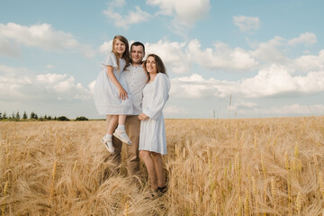 farmer carries little daughter in his arms through a field of wheat. happy child and father are playing in field of ripening wheat.Beautiful family in the park.