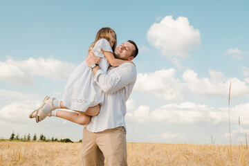 farmer carries little daughter in his arms through a field of wheat. happy child and father are playing in field of ripening wheat.Beautiful family in the park.