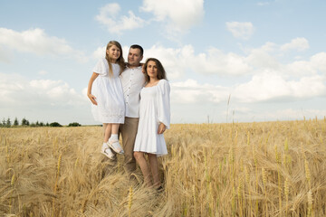 farmer carries little daughter in his arms through a field of wheat. happy child and father are playing in field of ripening wheat.Beautiful family in the park.
