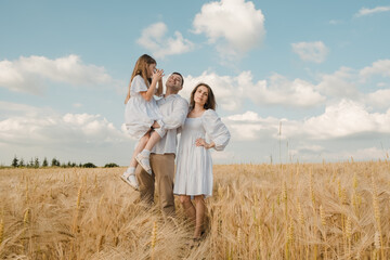 farmer carries little daughter in his arms through a field of wheat. happy child and father are playing in field of ripening wheat.Beautiful family in the park.