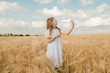 Beauty little girl outdoors enjoying nature wheat field. Beautiful girl in white dress running on the autumn field at sunset light.