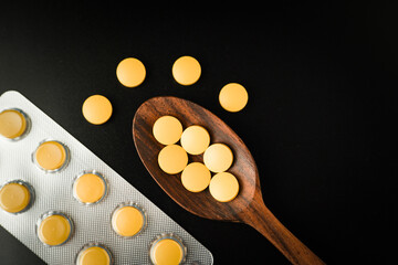 Pills Medicine tablet capsules blister pack in wooden spoon on a black background