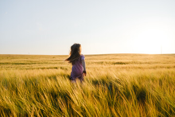 Happy child spends his childhood in the country, runs happily next to the wheat field. Child girl running through field of wheat, sunset.