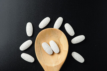 white Pills Medicine tablet capsules in a wooden spoon blister pack on a black background