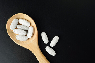 white Pills Medicine tablet capsules in a wooden spoon blister pack on a black background
