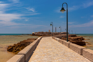Picturesque view of a stone causeway leading across the sandbank to the old fort Castillo de San Sebastian in Cadiz, Spain © Kavalenkava