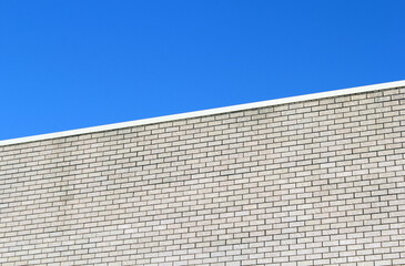 Light-colored brick wall of a building against a blue sky background textured abstract