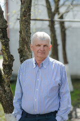 
One modern senior caucasian man portrait of male grandfather without a beard and hat cap stand in front of his house in day wear shirt happy confident copy space.