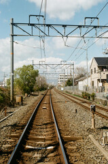 Fototapeta premium A long stretch of railway tracks in an urban area, framed by overhead electric wires and signaling equipment. The tracks extend into the distance, creating a sense of depth and perspective. 
