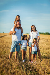 Mom, dad and  сute daughters hug in a wheat field. Beautiful children.Family vacation.Happy family resting in summer field.Cheerful family picnicking in the park.Summertime and vacation concept.