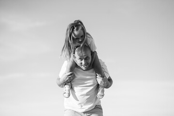 Dad and daughter playing in nature. Loving dad holds his daughter on his shoulders. Black and white photo.