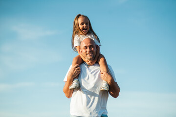 Dad with his daughter in his arms against the background of nature. They play together, laugh, hug and kiss.The child is on the father's neck.