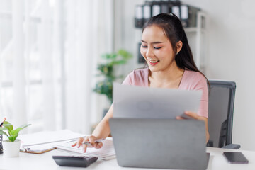 Asian Businesswoman Using laptop computer and working at office with calculator document on desk, doing planning analyzing the financial report, business plan investment, finance analysis concept.
