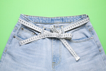 Jeans and measuring tape on green background, top view