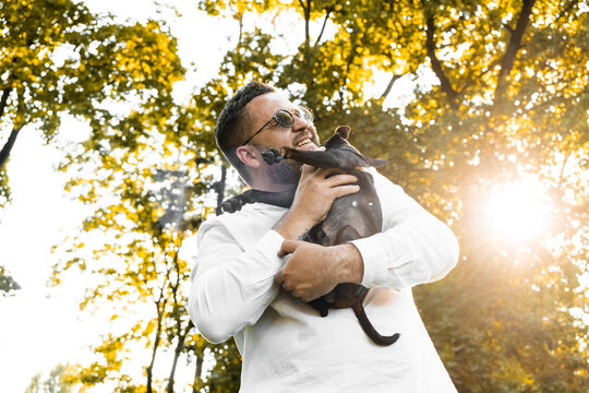 Black Man holds on his hands smiling  dog.Young man holding on hands his  dog, walking with cute puppy at summer day.