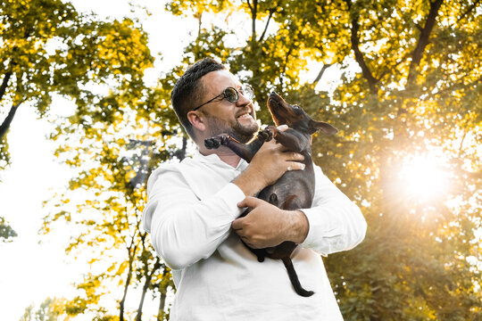 Black Man holds on his hands smiling  dog.Young man holding on hands his  dog, walking with cute puppy at summer day.