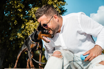 A guy kisses and hugs his puppy.Portrait of a handsome young man sitting in the park and hugging and kissing his beautiful dog.A dog and a man are playing together happily.
