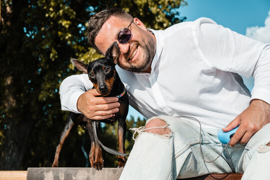 Black and Tan miniature pinscher female dog with owner in a park.A man plays with a pinscher dog.