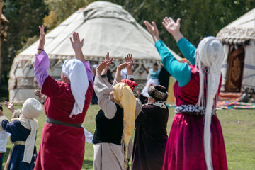 Women in traditional clothing perform a cultural ritual with raised arms in front of yurts at the...