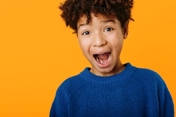 Joyful expression of a young african american boy with mouth wide open against a vibrant orange...