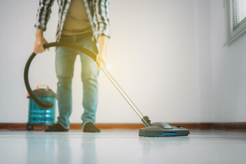 Fototapeta premium A Young man using vacuum cleaner is vacuuming the floor in the house, cleaning the house, modern living room.