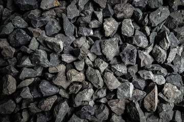 Close-up of various sizes of black gravel displayed on a flat surface for construction or...