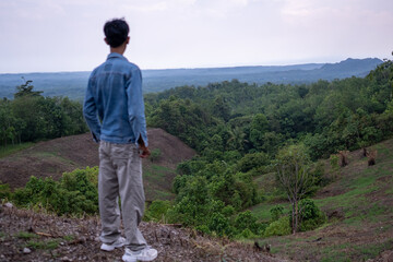 Fototapeta premium Man standing on a hillside overlooking green hills, reflective moment in nature, a sense of freedom and exploration.