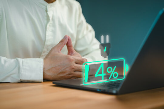Close-up of a person seated at a desk with a laptop showing a low battery icon at 4%, symbolizing power shortage or urgency. Person appears to be waiting, possibly for the device to charge.