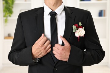 Groom in suit with stylish boutonniere indoors, closeup
