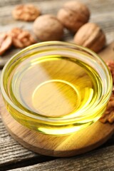 Cooking oil in bowl and walnuts on wooden table, closeup