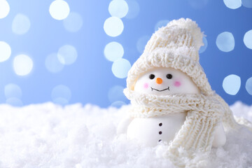 Cute decorative snowman on artificial snow against light blue background, space for text