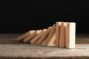 Domino effect. Wooden blocks falling on table against black background, closeup