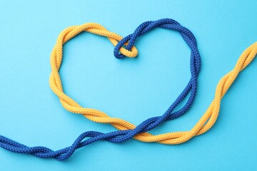 Heart made of tied ropes on light blue background, top view. Unity concept