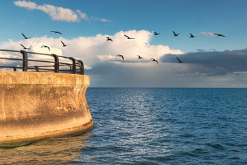 An old curved concrete sea wall with a black railing with small waves  on teh ater and a dramatic...