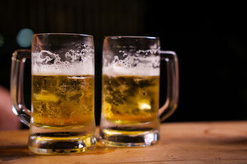 Two frothy pints of beer sit on a wooden bar counter, creating a warm, inviting pub atmosphere. Perfectly chilled with a golden glow, they evoke a sense of relaxation and camaraderie.
