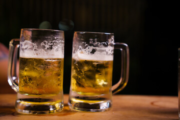 Two frothy pints of beer sit on a wooden bar counter, creating a warm, inviting pub atmosphere. Perfectly chilled with a golden glow, they evoke a sense of relaxation and camaraderie.