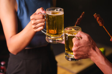 Close-up of friends clinking glasses of beer, celebrating together at a bar.The lively atmosphere captures laughter, camaraderie,good times, as young friends enjoy a night out with refreshing drinks