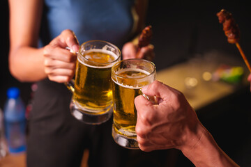 Close-up of friends clinking glasses of beer, celebrating together at a bar.The lively atmosphere captures laughter, camaraderie,good times, as young friends enjoy a night out with refreshing drinks