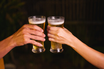 Close-up of friends clinking glasses of beer, celebrating together at a bar.The lively atmosphere captures laughter, camaraderie,good times, as young friends enjoy a night out with refreshing drinks