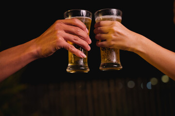 Close-up of friends clinking glasses of beer, celebrating together at a bar.The lively atmosphere captures laughter, camaraderie,good times, as young friends enjoy a night out with refreshing drinks