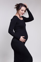 Portrait of young pregnant female in black dress with hands near pregnant belly.