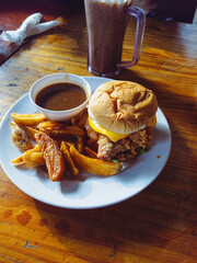 Classic cheeseburger with baked potatoes served on a white plate on a wooden table.