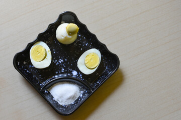 Hard boiled egg cutting in half and salt put on a small black plate isolated white background....