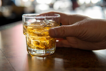 Male hand holding a glass of whiskey on ice