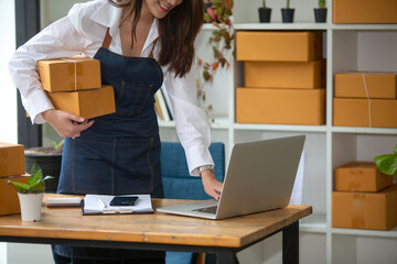 Beautiful business woman Happy working online shopping at her store. Through phone, computer, young woman seller prepares parcel boxes to send to customers. online sales ecommerce