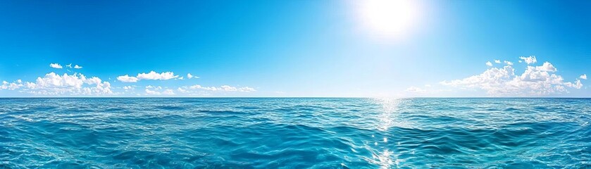 Obraz premium A stunning panoramic view of a serene ocean under a bright blue sky, featuring gentle waves reflecting sunlight and fluffy clouds in the distance.