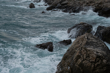 Turquoise sea stone beach, breaking waves on a cloudy spring day. Beautiful sea background. The concept of summer, vacation, travel. The purest clear sea water, large stones on the beach close-up