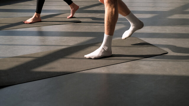 Yoga group. Aerobic workout. Unrecognizable active people stepping barefoot on sport mat before star pilates class training session in gym studio indoors.