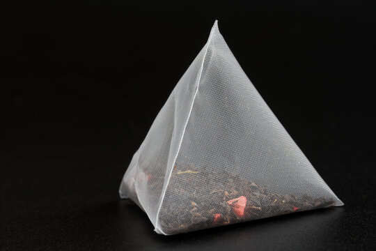 Triangular pyramid tea bag with black flavored tea, with added fruits and berries, on a dark background. Photo. Selective focus