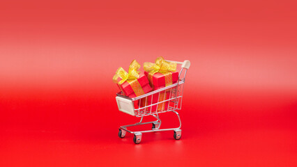 Supermarket trolley, with red gifts. Buying gifts for Sale, Discounts, Black Friday, New Year, Christmas, Birthday and Valentines day. On a red background, minimal design banner